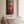Red Buddha canvas art in a black frame, hung above a freestanding bathtub in a bright travertine bathroom | MusaArtGallery™